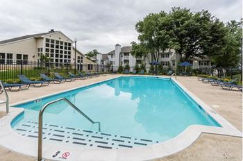 A swimming pool with chaise lounge chairs and apartment buildings in the background